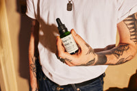 Pomp & Co. Beard Oil, homme tenant le flacon en verre vert